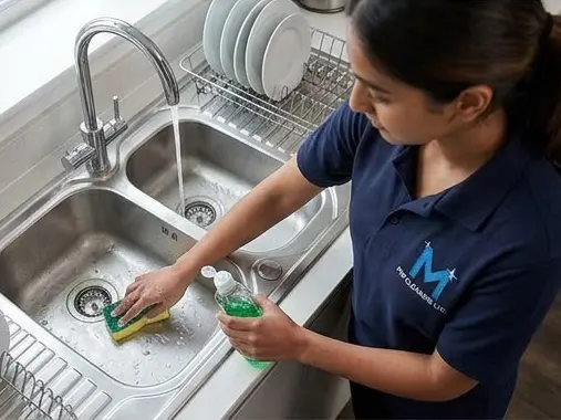 Team member scrubbing a stainless steel kitchen sink